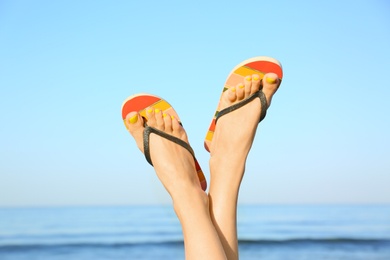 Photo of Closeup of woman wearing flip flops near sea, space for text. Beach accessories