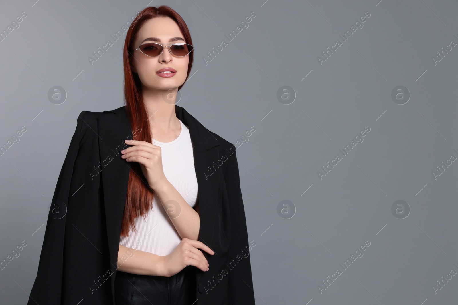 Photo of Stylish woman with red dyed hair and sunglasses on light gray background, space for text