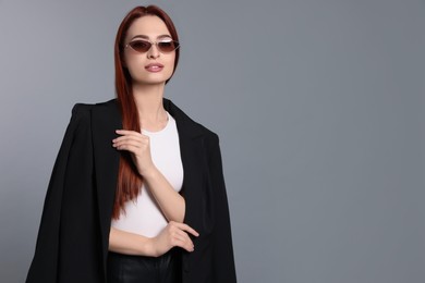 Photo of Stylish woman with red dyed hair and sunglasses on light gray background, space for text
