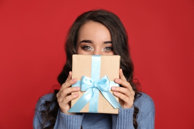 Beautiful young woman with Christmas gift on red background