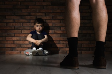 Adult man without pants standing in front of despaired little boy indoors. Child in danger