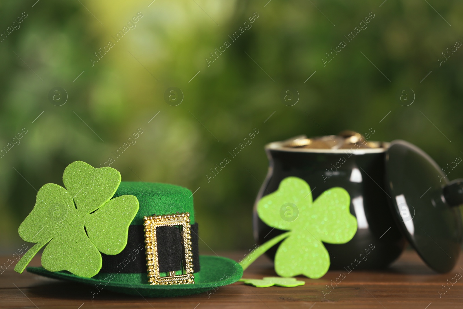 Photo of Leprechaun hat, clover leaves and pot of gold on wooden table against blurred background, space for text. St Patrick's Day celebration