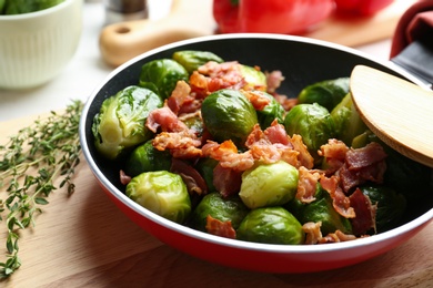 Photo of Tasty roasted Brussels sprouts with bacon on cutting board, closeup