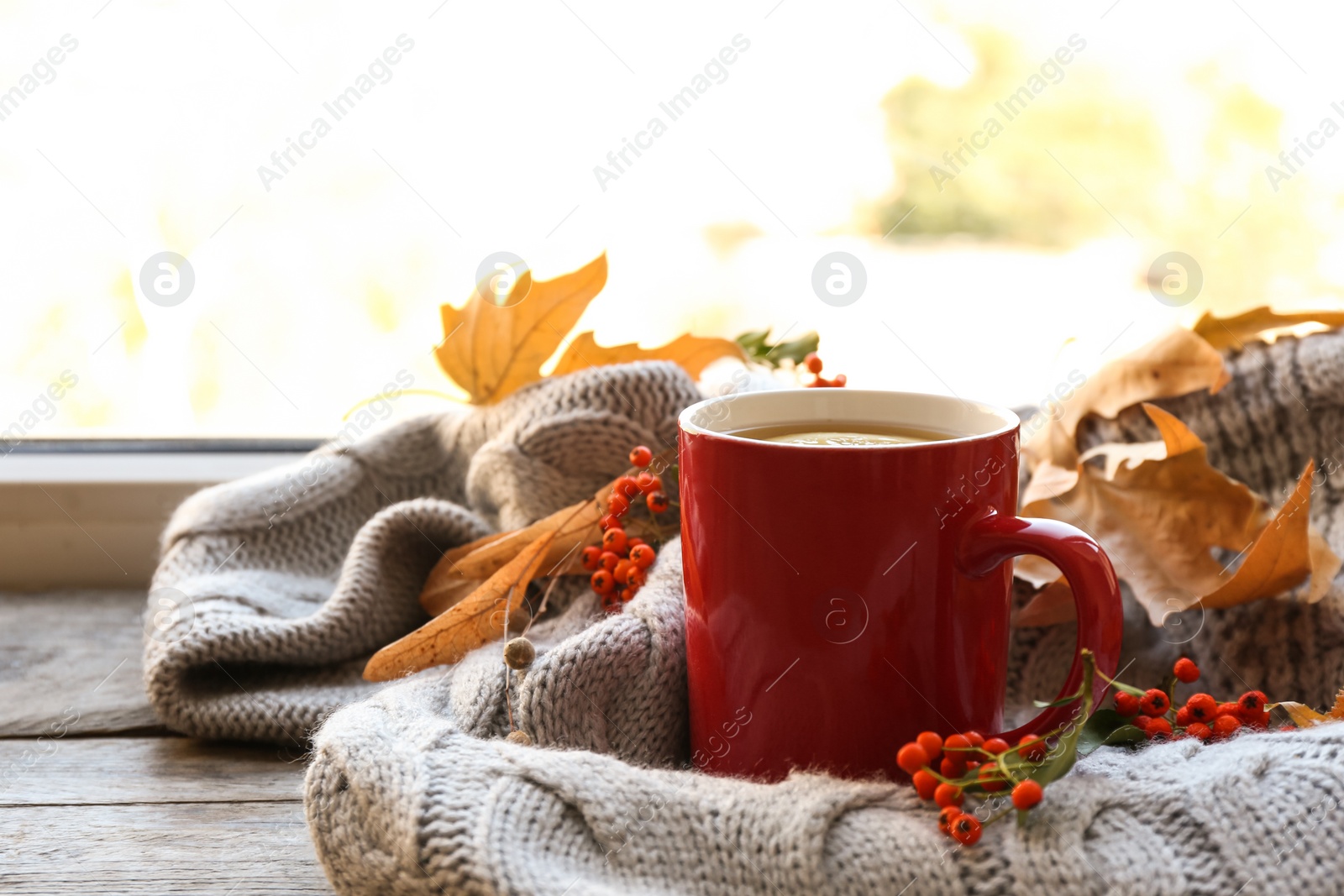 Photo of Cup of hot drink, sweater and autumn leaves on windowsill, space for text. Cozy atmosphere