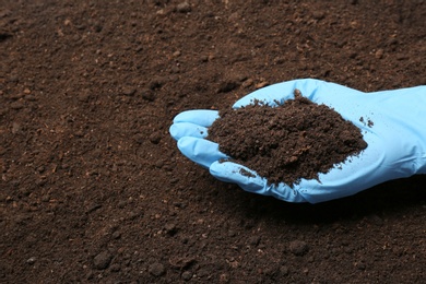 Scientist holding pile of soil above ground, closeup. Space for text