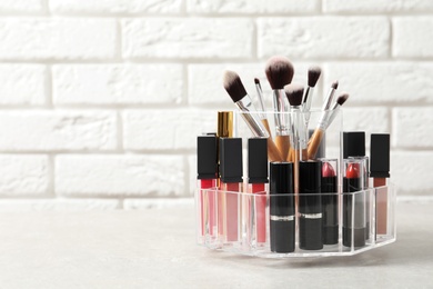 Photo of Lipstick holder with different makeup products on table against brick wall. Space for text