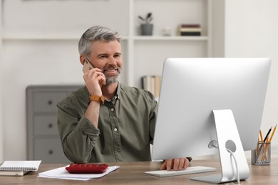 Professional accountant talking on phone and working at wooden desk in office