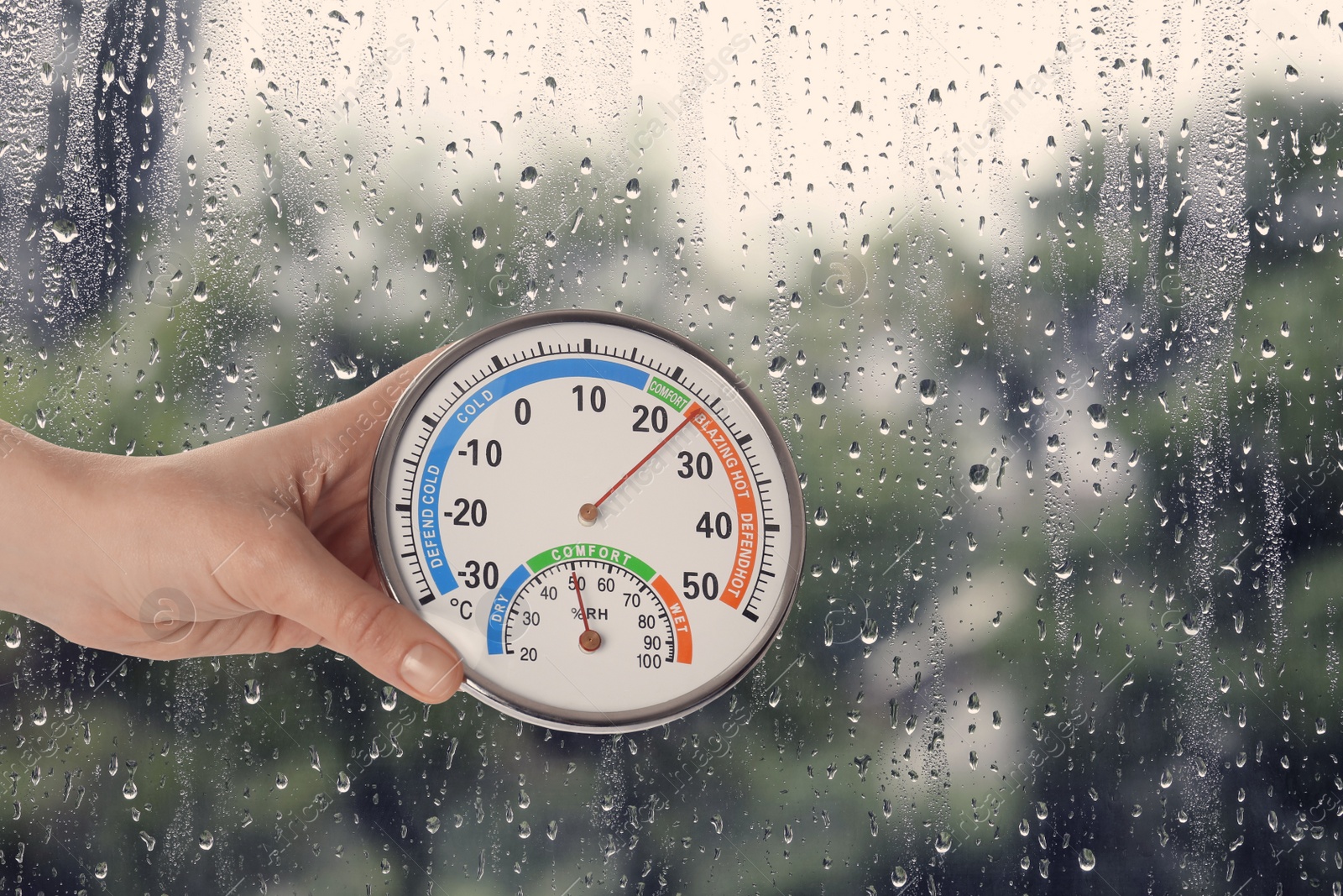 Image of Woman holding hygrometer with thermometer near window on rainy day, closeup