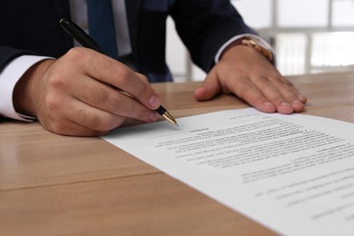 Businessman signing contract at wooden table indoors, closeup