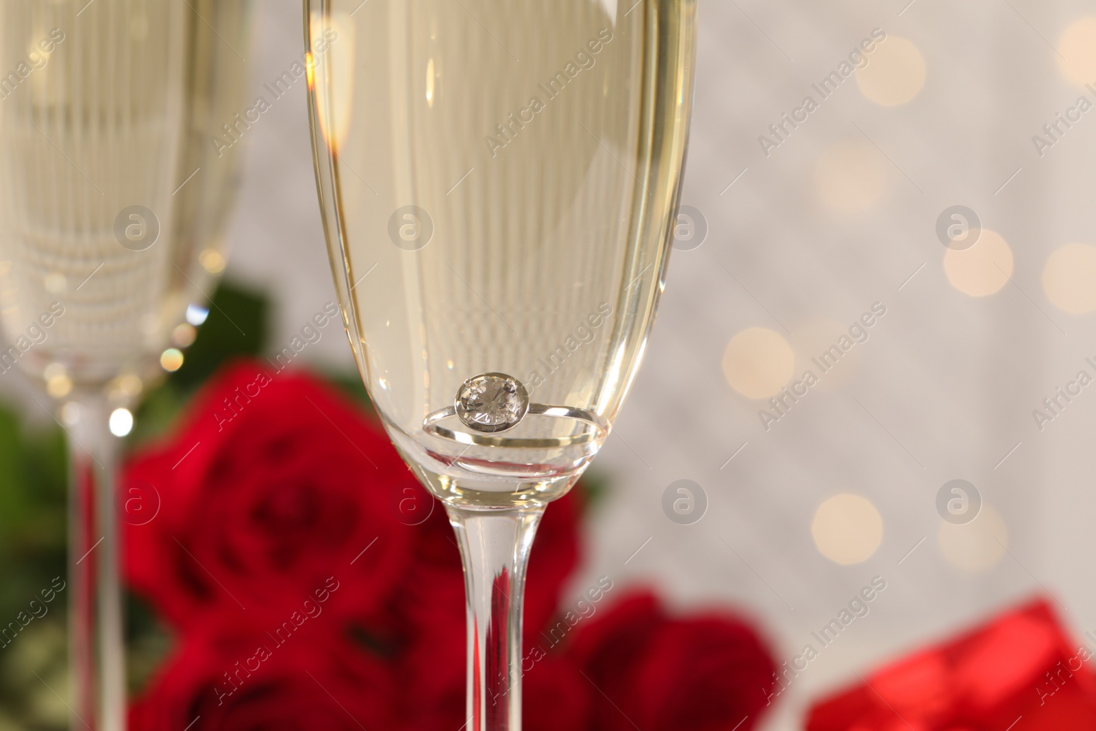 Photo of Beautiful engagement ring with gemstone in glass of sparkling wine, closeup