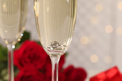 Photo of Beautiful engagement ring with gemstone in glass of sparkling wine, closeup