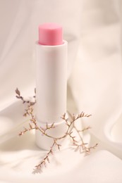 Photo of Lip balm on white fabric, closeup. Cosmetic product