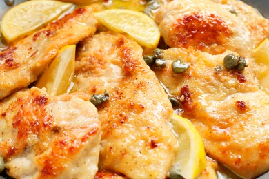 Photo of Delicious chicken piccata with lemons as background, closeup