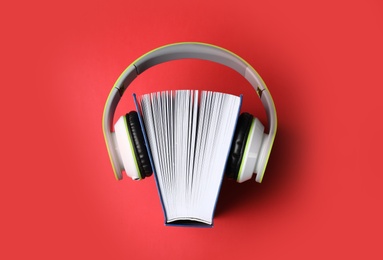 Photo of Modern headphones with hardcover book on color background, top view