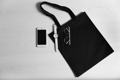 Photo of Flat lay composition with eco tote bag, smartphone and accessories on white wooden background. Space for design
