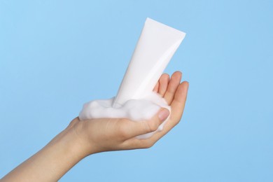 Photo of Woman with tube of care product and cleansing foam on light blue background, closeup