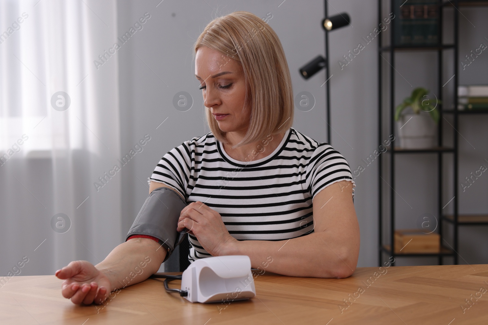 Photo of Woman measuring her blood pressure with tonometer at wooden table indoors