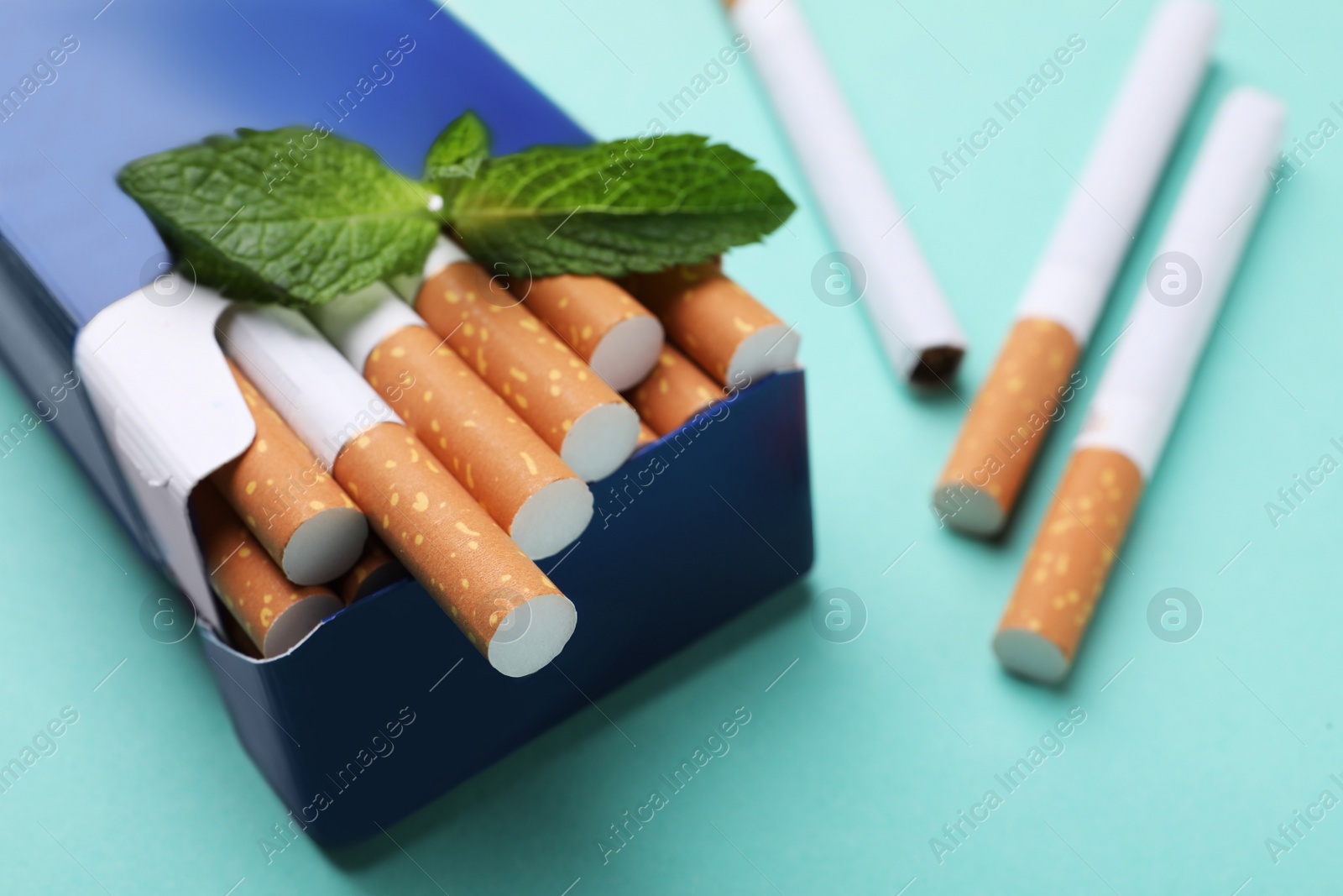 Photo of Pack of menthol cigarettes and mint on turquoise background, closeup. Space for text