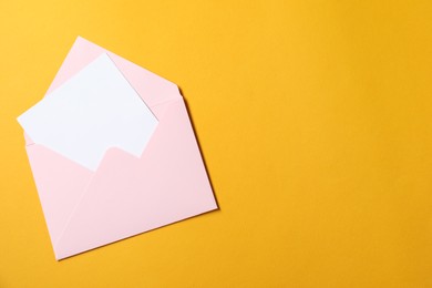 Photo of Blank sheet of paper in open letter envelope on orange background, top view. Space for text