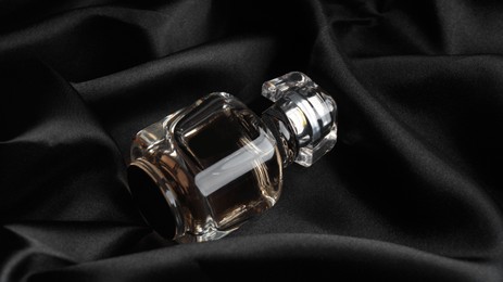 Photo of Luxury bottle of perfume on black silk, closeup