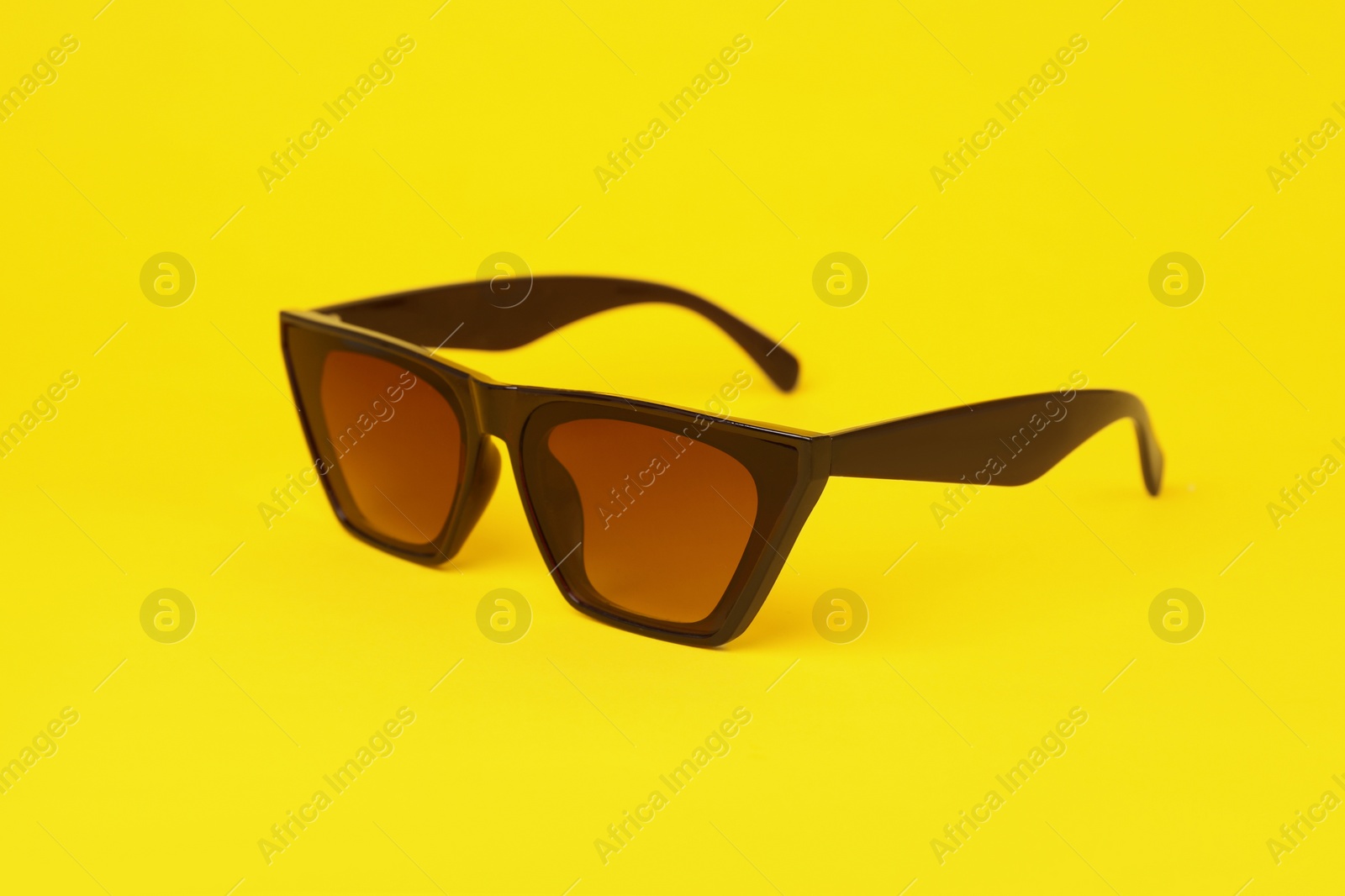 Photo of Stylish pair of sunglasses on yellow background