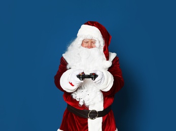 Photo of Authentic Santa Claus with game controller on blue background. Space for text