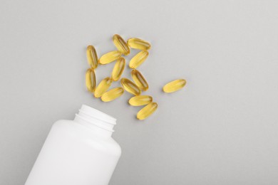 Photo of Bottle and vitamin capsules on light grey background, top view. Space for text