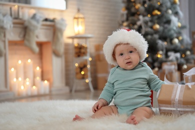 Cute baby wearing Santa hat in room with Christmas tree