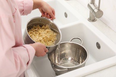 Woman draining pasta into colander at sink, closeup