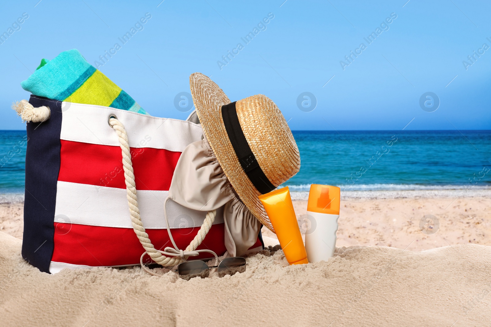 Image of Bag with bikini and accessories on sunny ocean beach, space for text. Summer vacation