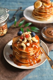 Photo of Stack of tasty pancakes with berries, nuts and syrup on table