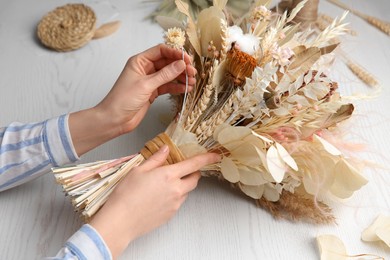 Florist making beautiful bouquet of dried flowers at white table, closeup