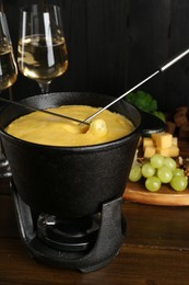 Dipping different products into fondue pot with melted cheese on wooden table