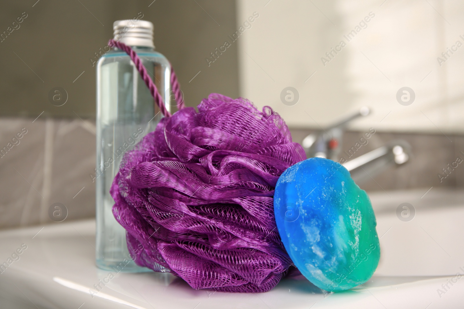 Photo of Purple shower puff and cosmetic products on sink in bathroom