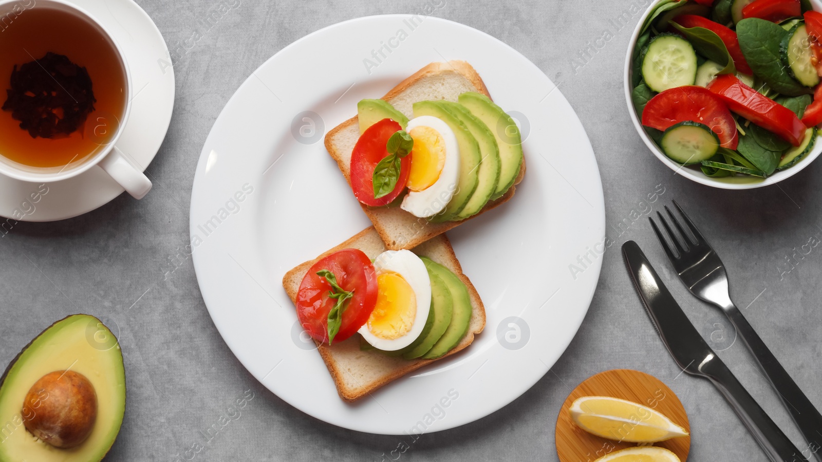 Photo of Tasty sandwiches with boiled egg, avocado and tomato served on grey table, flat lay