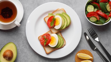 Photo of Tasty sandwiches with boiled egg, avocado and tomato served on grey table, flat lay