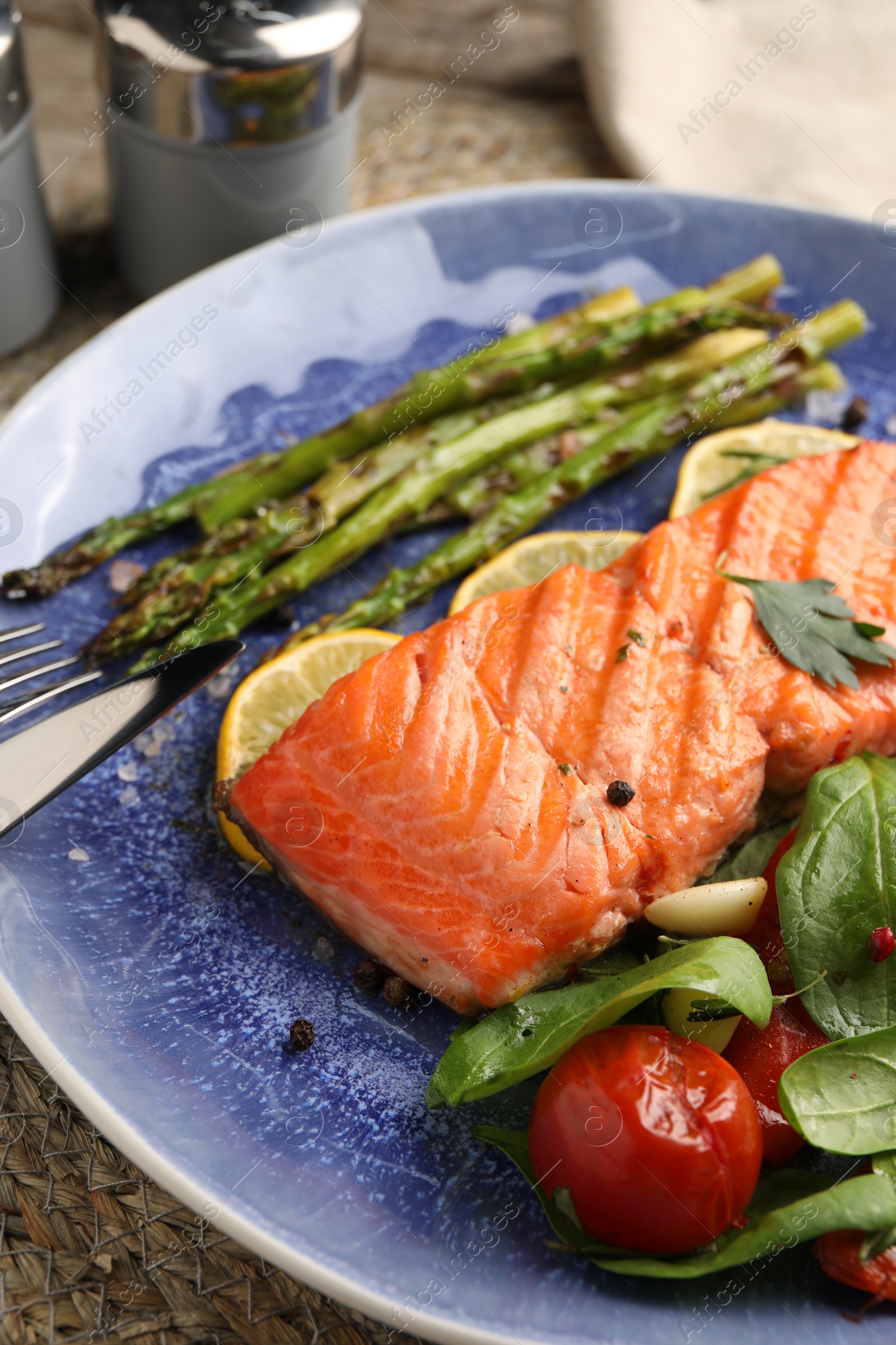 Photo of Tasty grilled salmon with tomatoes, asparagus, spinach and lemon served on table, closeup