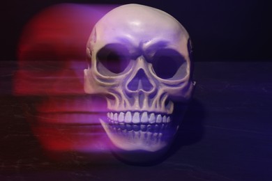 Photo of Human skull in neon lights on dark grey table