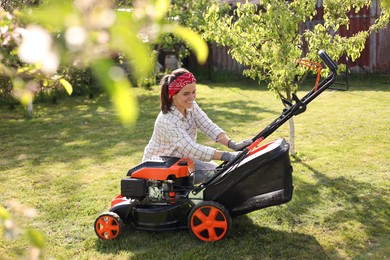 Smiling woman with lawn mower in garden on sunny day