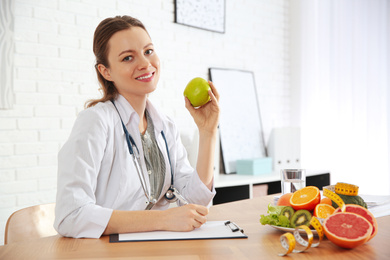 Photo of Nutritionist with apple and clipboard at desk in office
