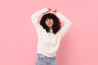 Happy young woman in stylish white sweater on pink background