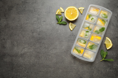 Photo of Ice cubes with lemon and mint in tray on grey table, flat lay. Space for text