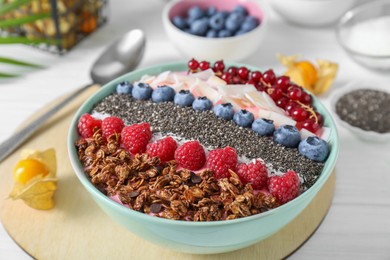 Photo of Tasty smoothie bowl with fresh berries and granola served on white table