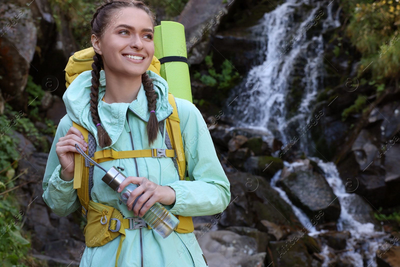 Photo of Tourist with backpack and bottle near waterfall in mountains. Space for text