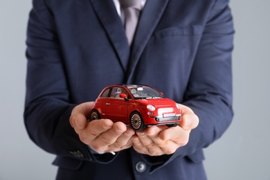 Photo of Male insurance agent holding toy car on grey background, closeup