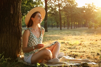 Young woman reading book on green grass near tree in park