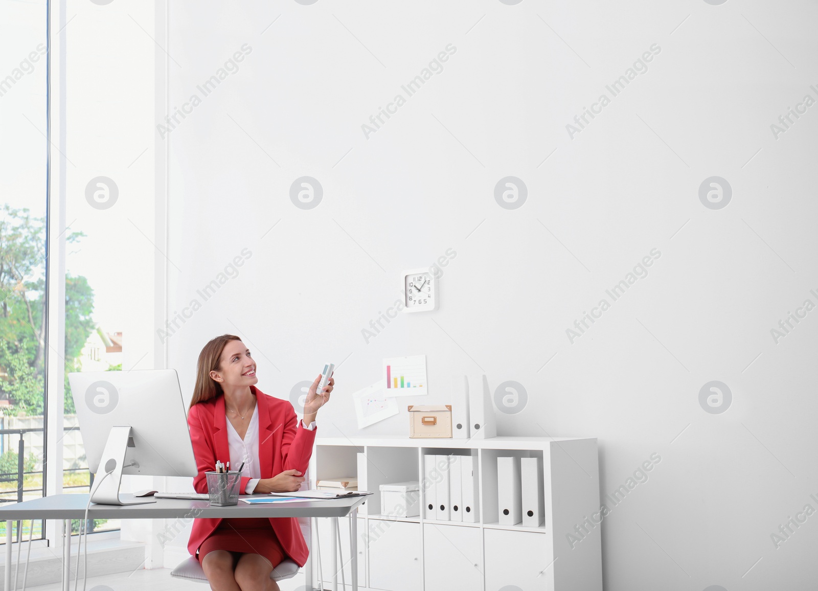 Photo of Happy young woman operating air conditioner with remote control in office