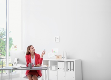 Happy young woman operating air conditioner with remote control in office