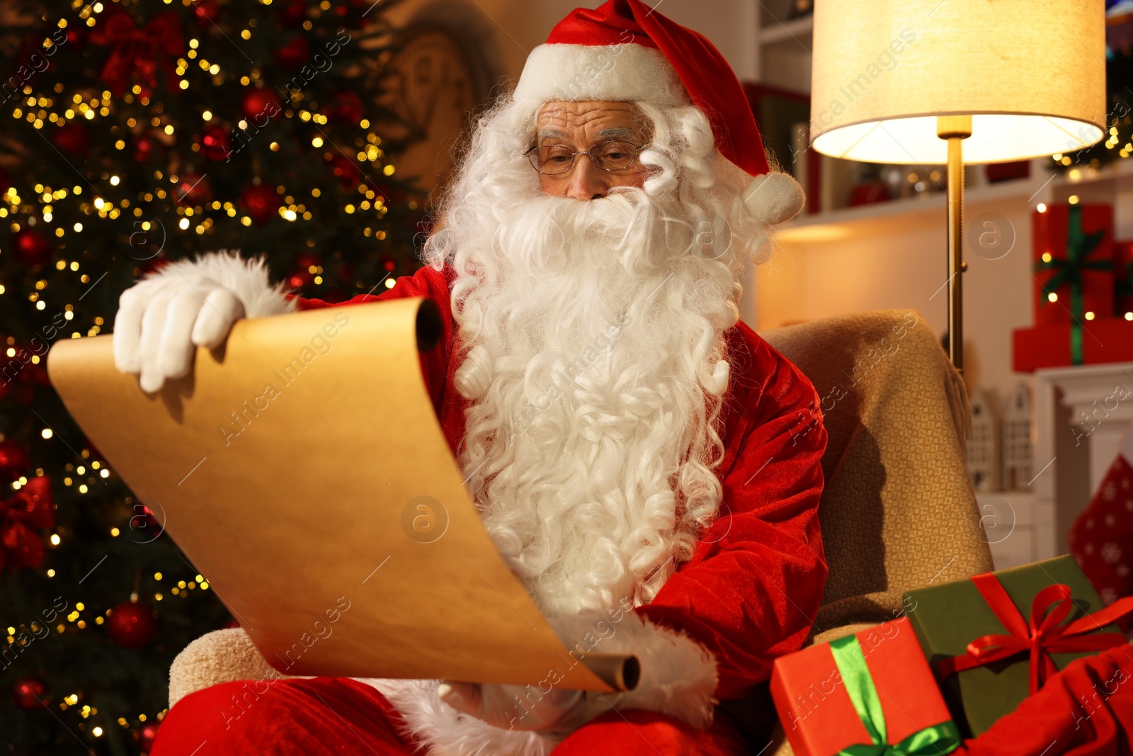 Photo of Santa Claus reading letter in room with Christmas tree