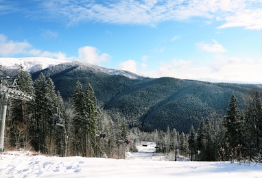 Beautiful mountain landscape with forest and ski lift on sunny day in winter